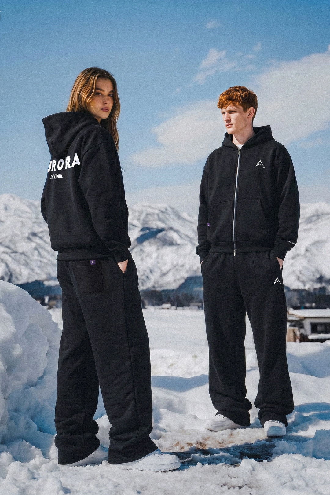 Two people wearing black outfits with visible branding in a snowy landscape.