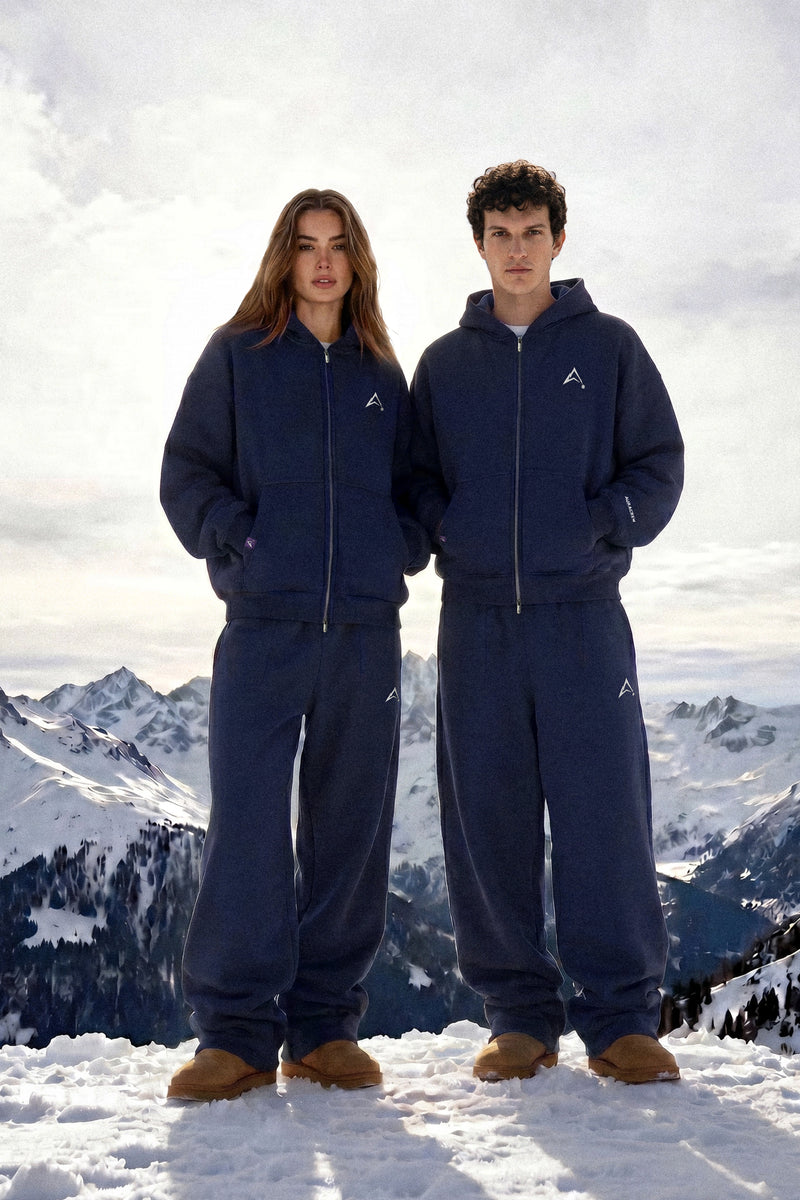 Two people wearing blue snow suits standing on a snowy mountain