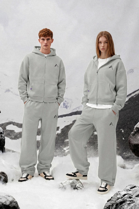 Two people wearing matching gray tracksuits standing in a snowy landscape.