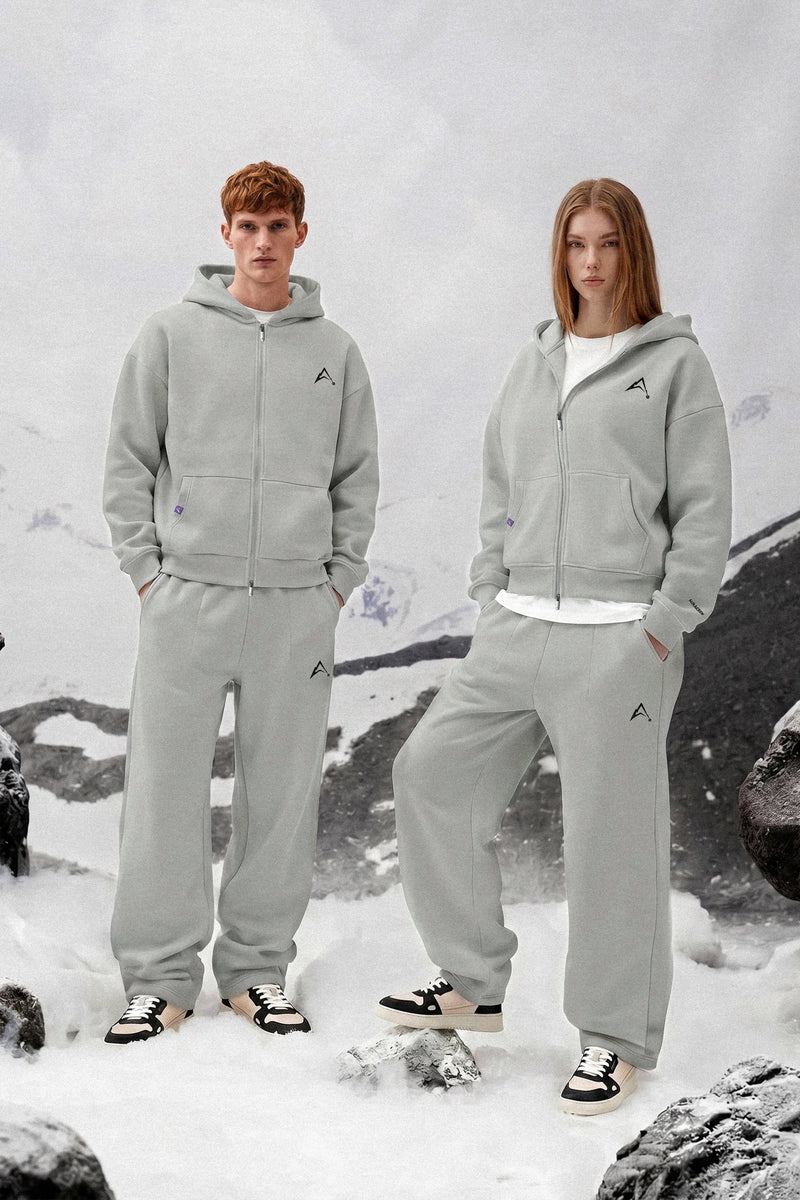 Two people wearing matching gray tracksuits standing in a snowy landscape.