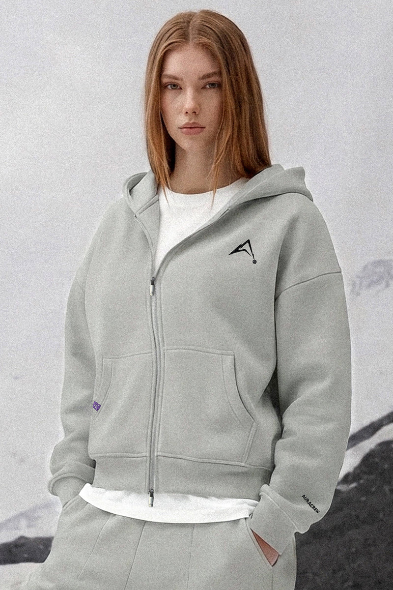 Person wearing a gray hoodie with a logo on a textured gray background
