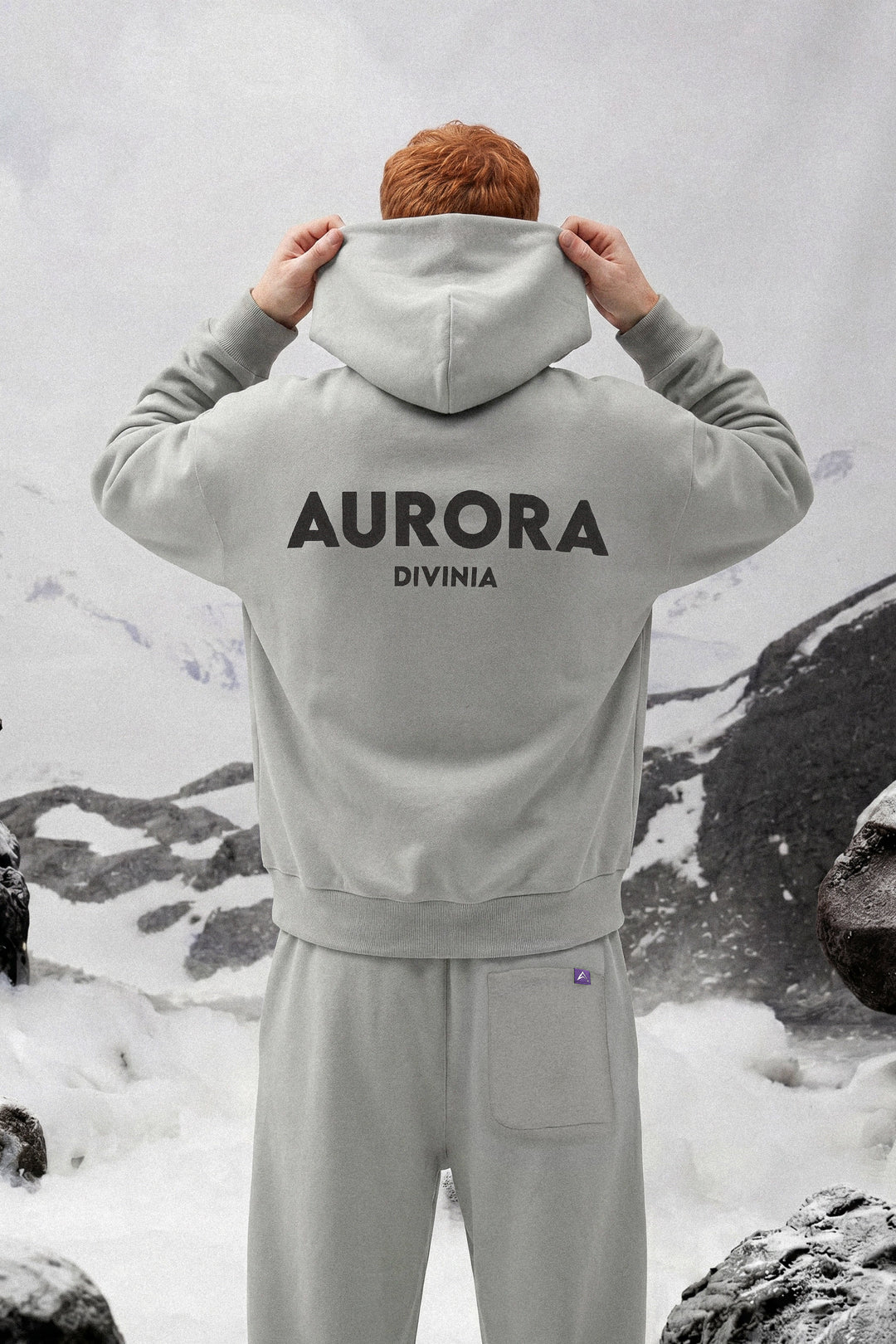 Person wearing a gray hoodie with 'AURORA DIVINIA' text in a snowy landscape