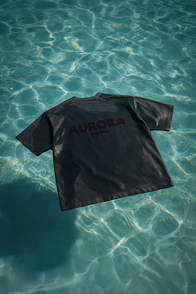 Black t-shirt with 'AURORA DIVINIA' branding on a clear blue water surface