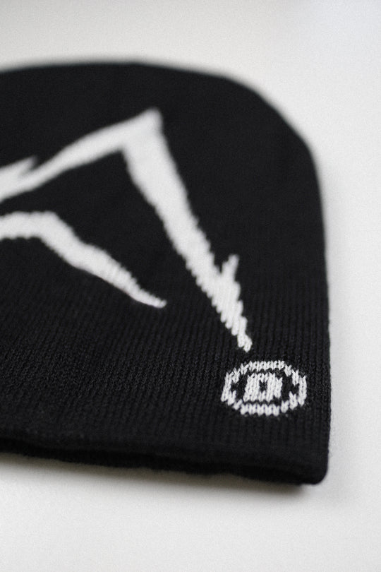 A close-up of a black knit beanie featuring a white knit mountain graphic and a small white circular logo with a stylized letter 'D' on the side, set against a plain light background.