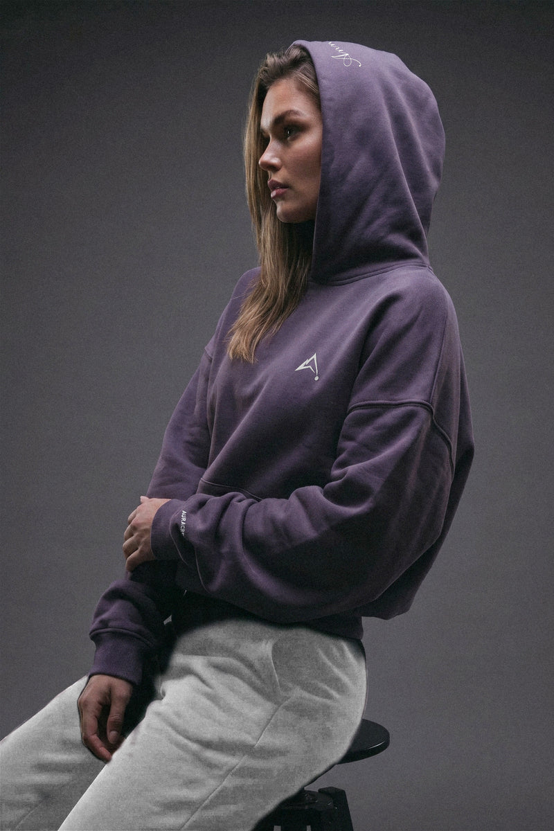 Aurora Divinia Anniversary Purple Hoodie — model wearing deep purple oversized hoodie with Aurora Divinia logo, styled with grey sweatpants