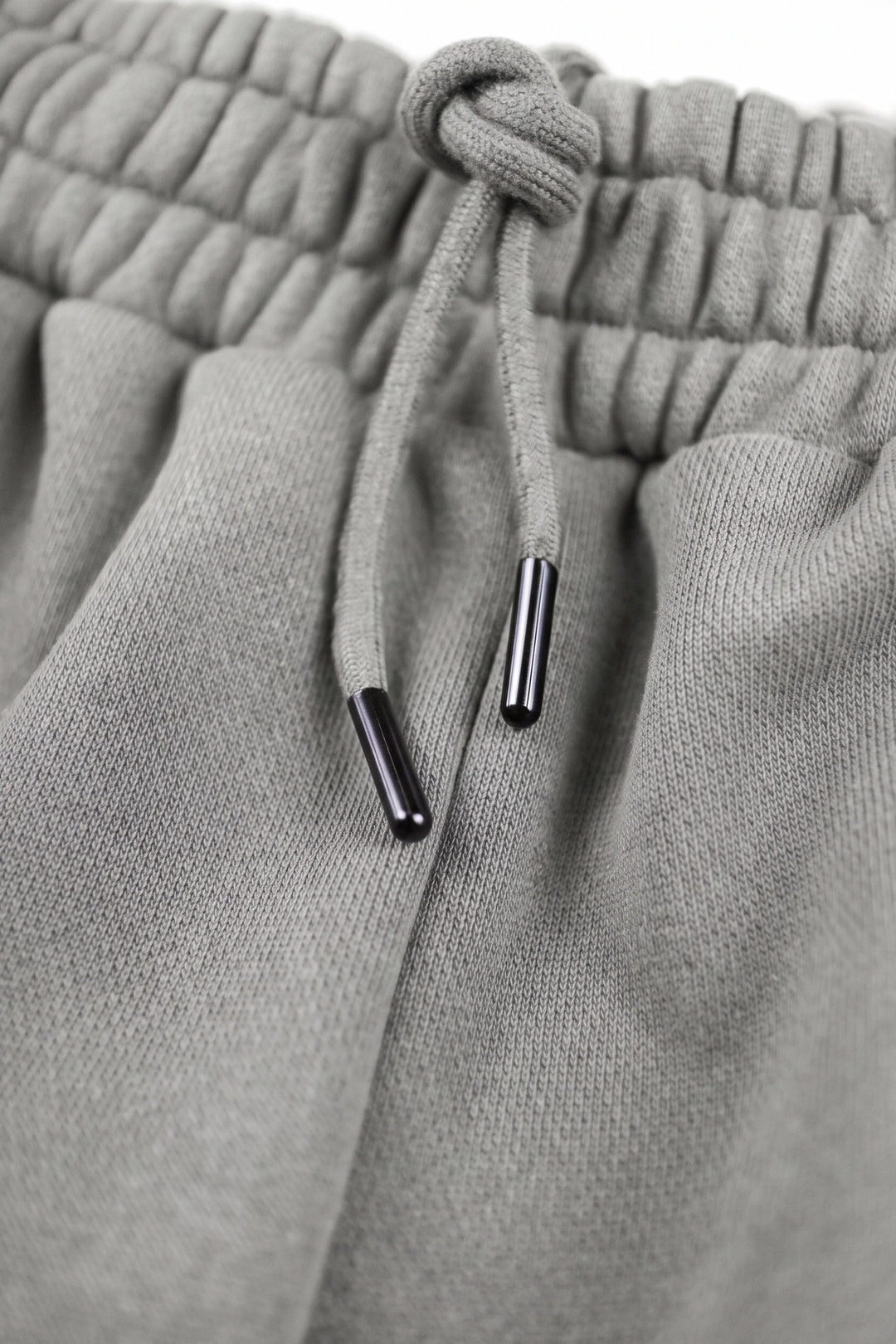 Close-up of light gray knit sweatpants showing the elasticized drawstring waistband and black drawstring tips.