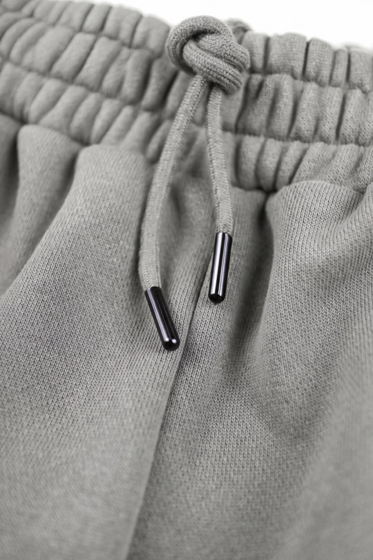 Close-up of light gray knit sweatpants showing the elasticized drawstring waistband and black drawstring tips.