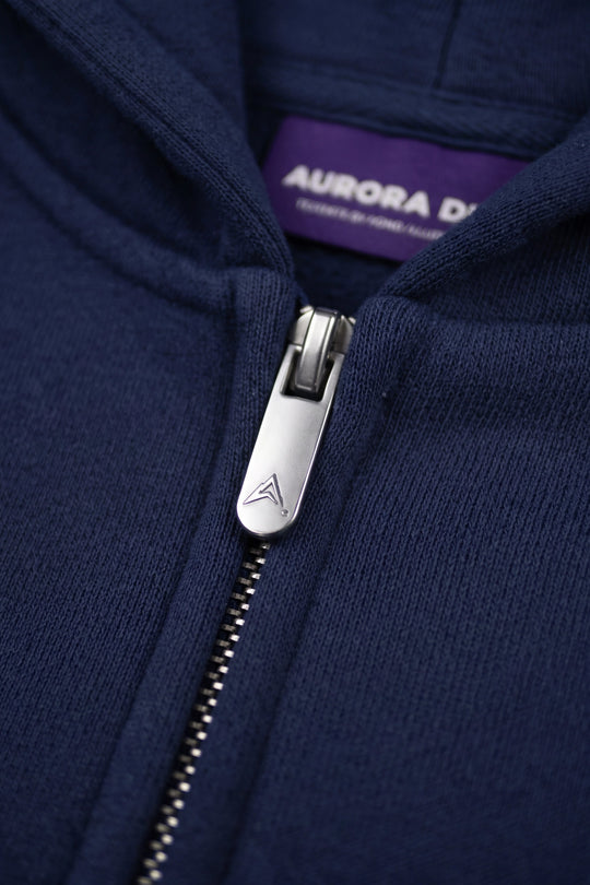 Close-up of a navy blue zip-up hoodie with a silver metal zipper pull and a purple interior neck label reading AURORA DESIGN.