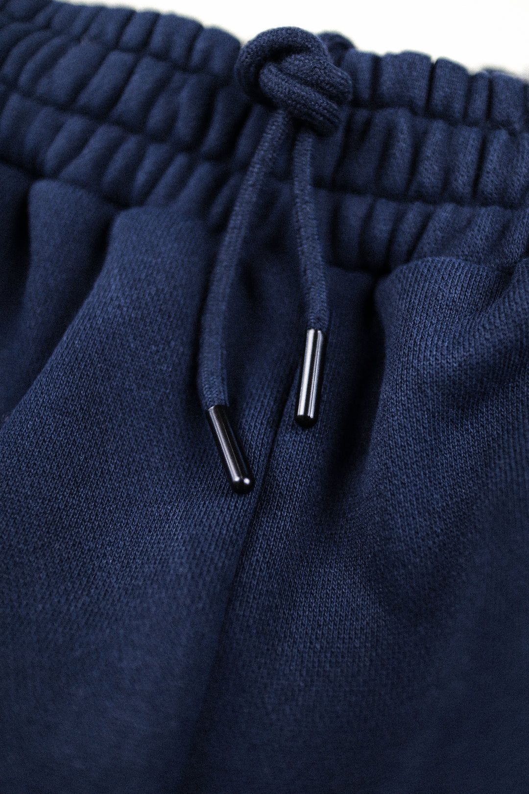 Close-up of navy blue knit drawstring pants showing the textured fabric, elastic waistband, and black drawstring tips.
